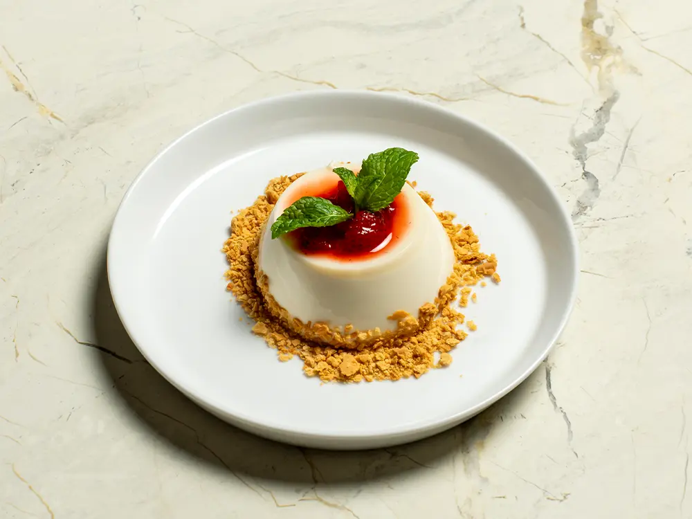Restyled panna cotta with strawberry compote, mint, and a biscuit-crumble base on a clean white plate over marble.